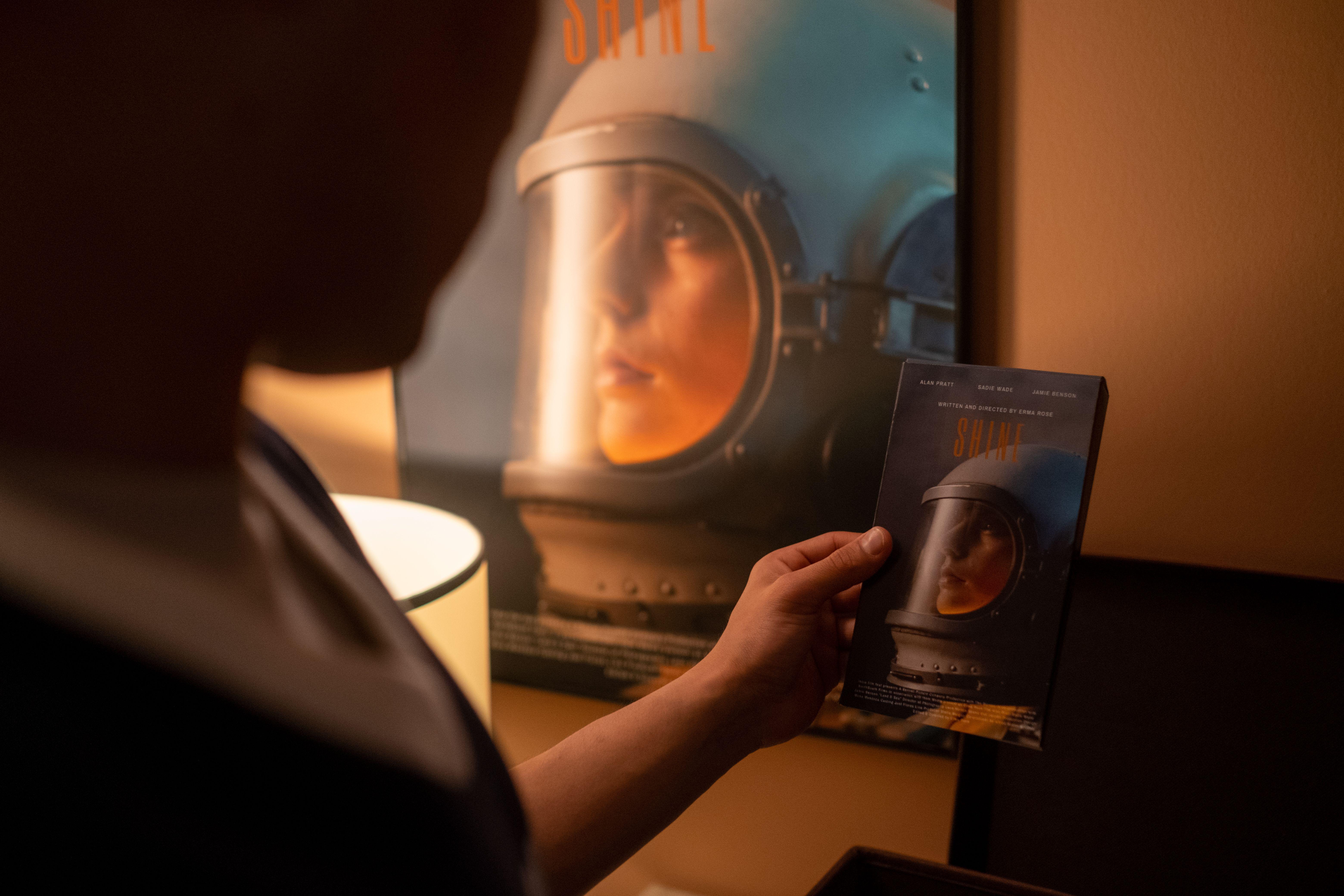 Person holding a VHS tape in front of a vintage film poster in a dimly lit room.
