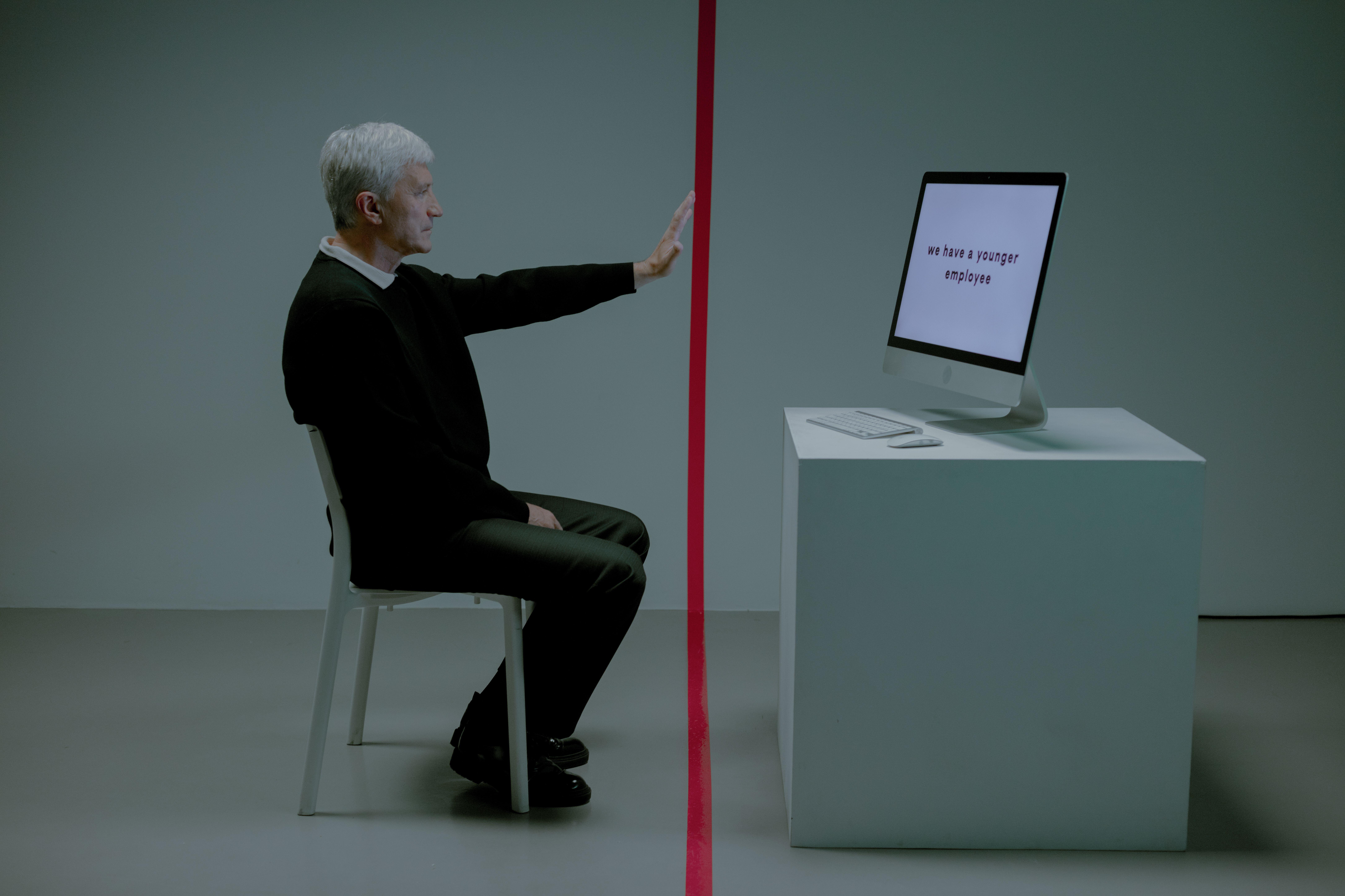 Senior man facing age discrimination in workplace, seated opposite a computer.