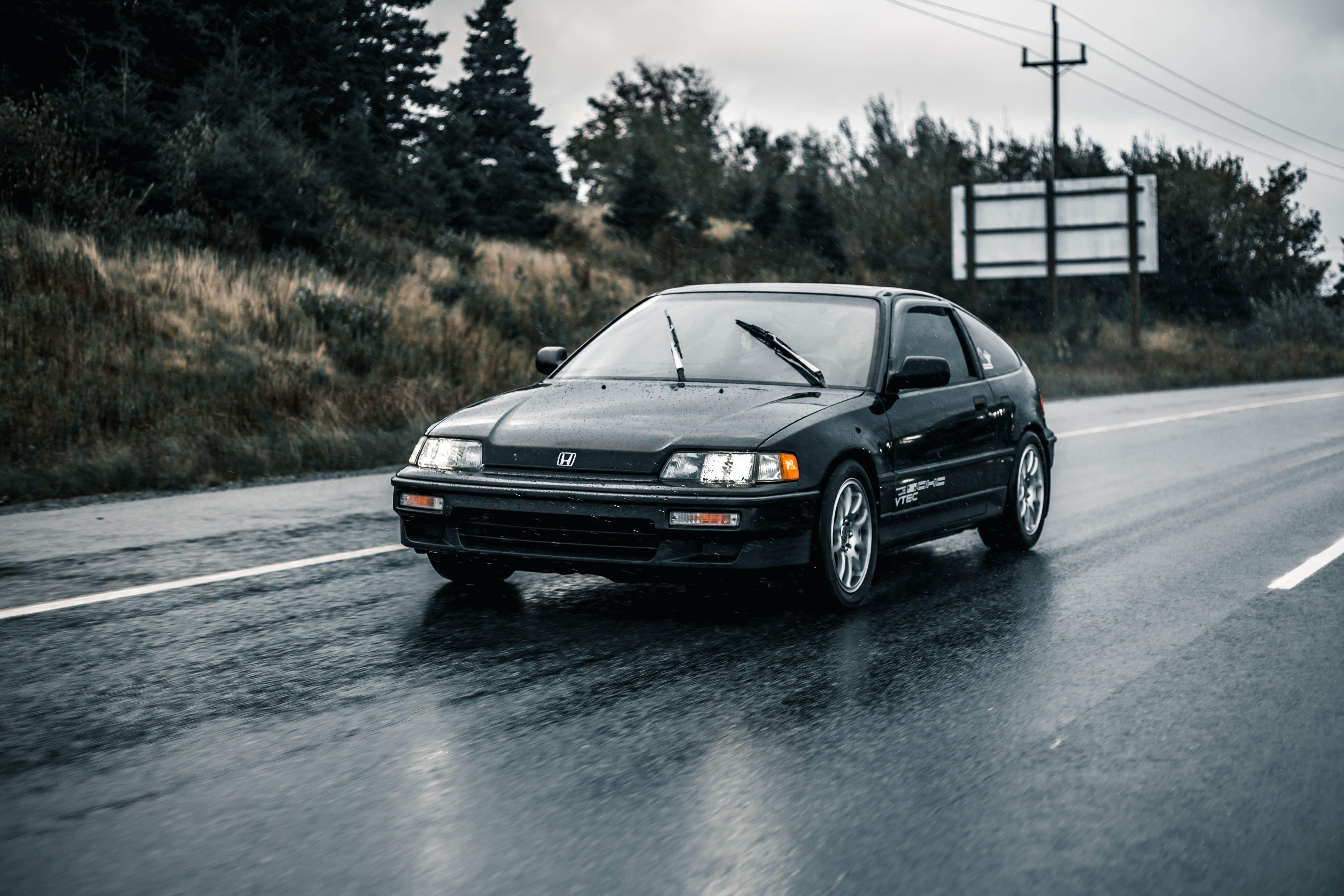 Black Honda car driving on wet road during rain, showcasing transportation in action.