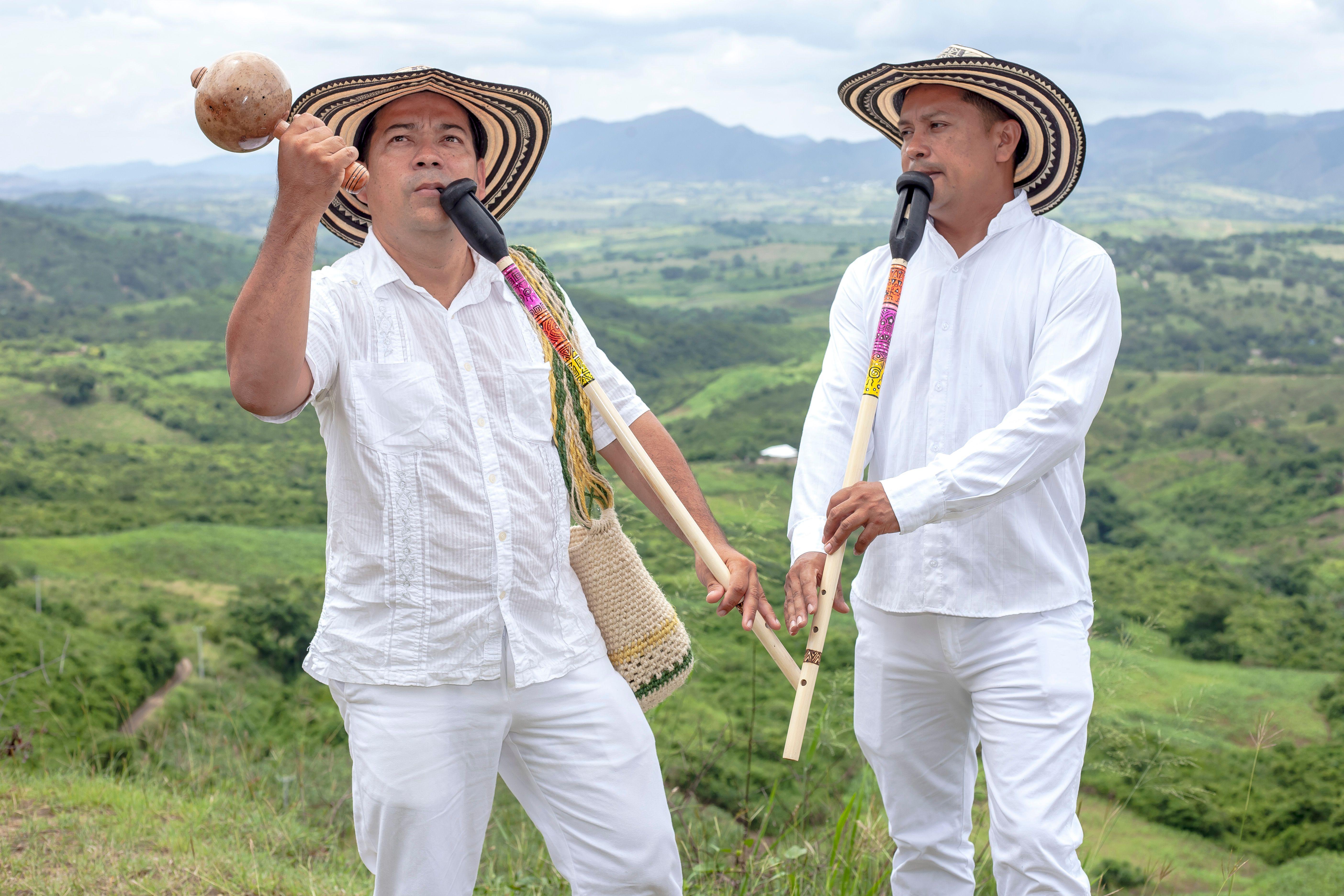 Men playing traditional flutes in the vibrant landscape of Ovejas, Colombia, showcasing cultural heritage.