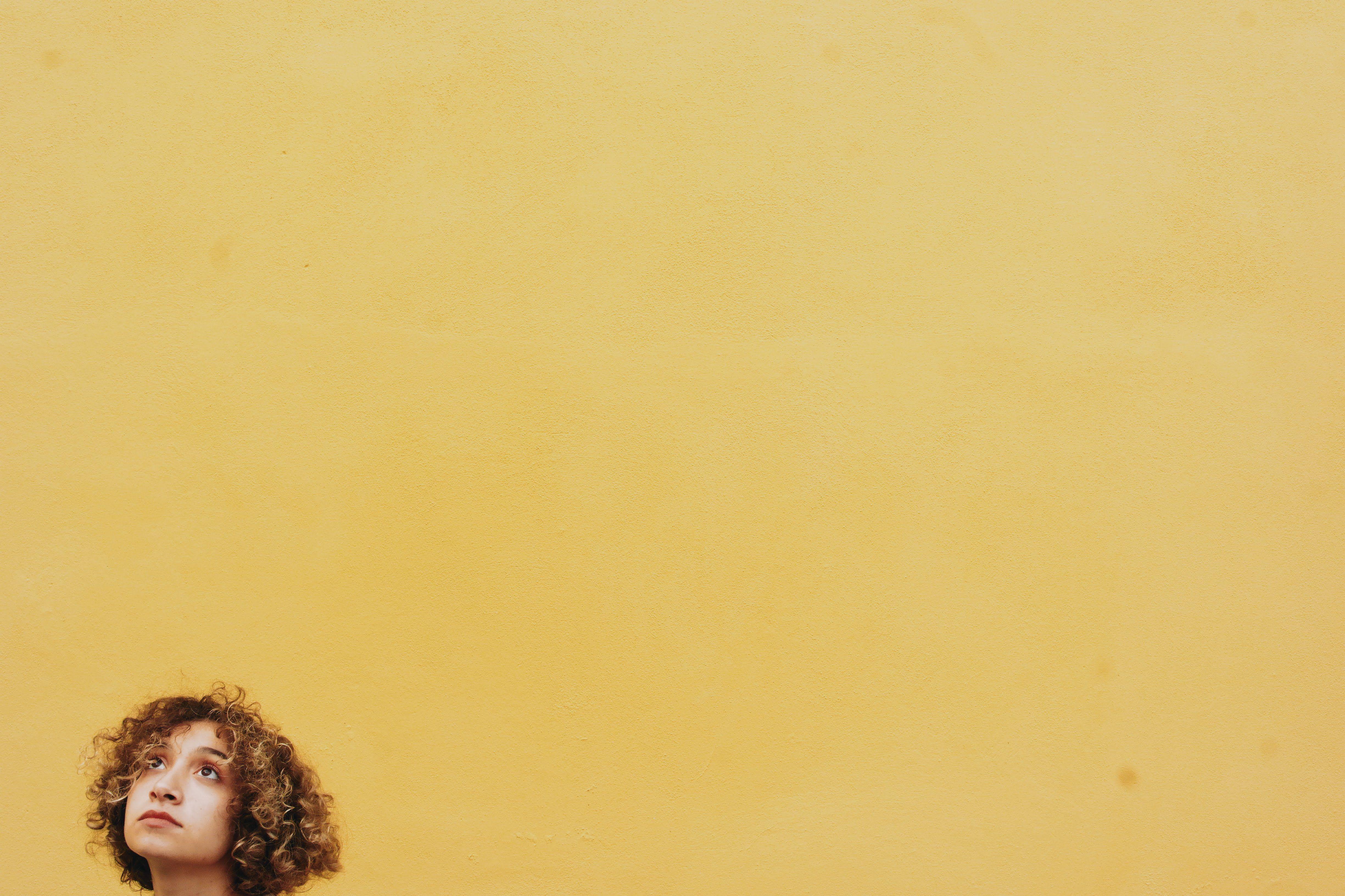 Portrait of a curly-haired woman looking up against a vibrant yellow background with space for text.