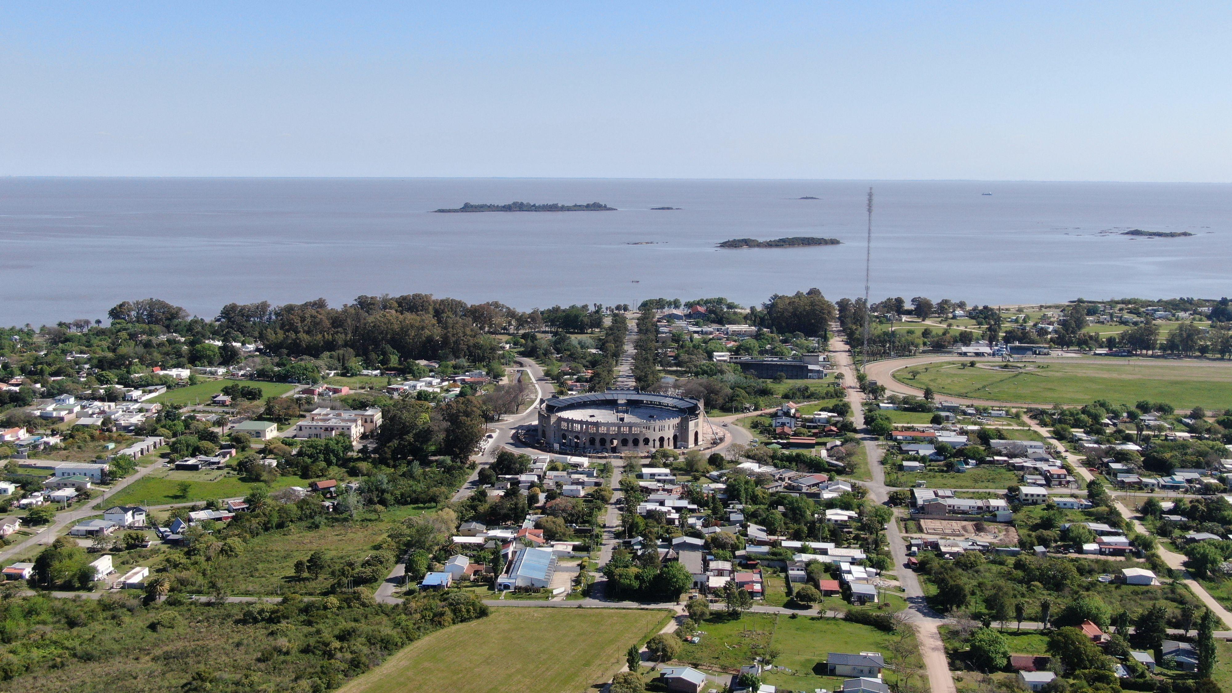 Aerial view of Colonia Del Sacramento, featuring the coast and Plaza de Toros with lush greenery.