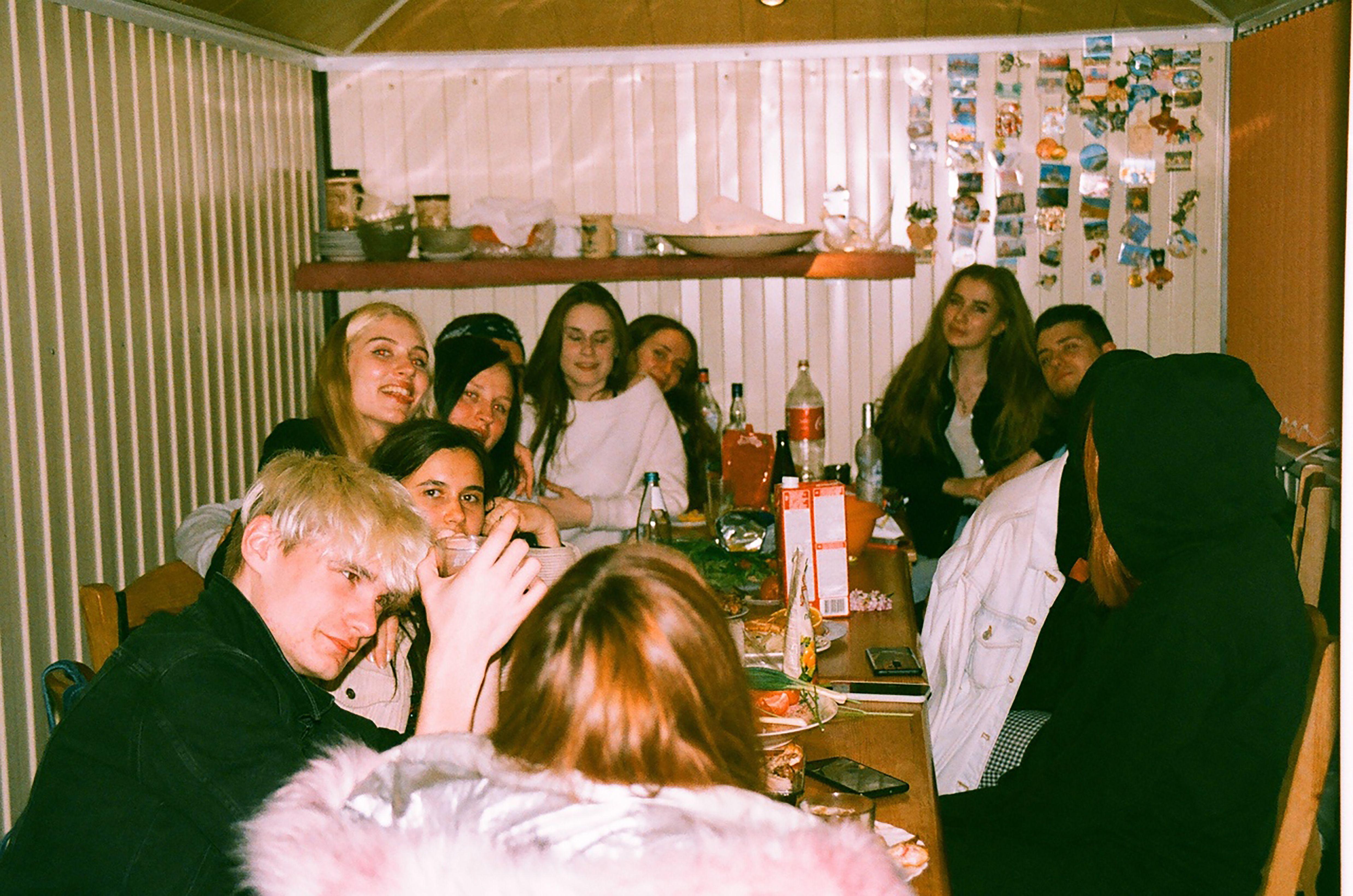 A group of young friends enjoy a casual indoor gathering at night, sharing food and drinks.