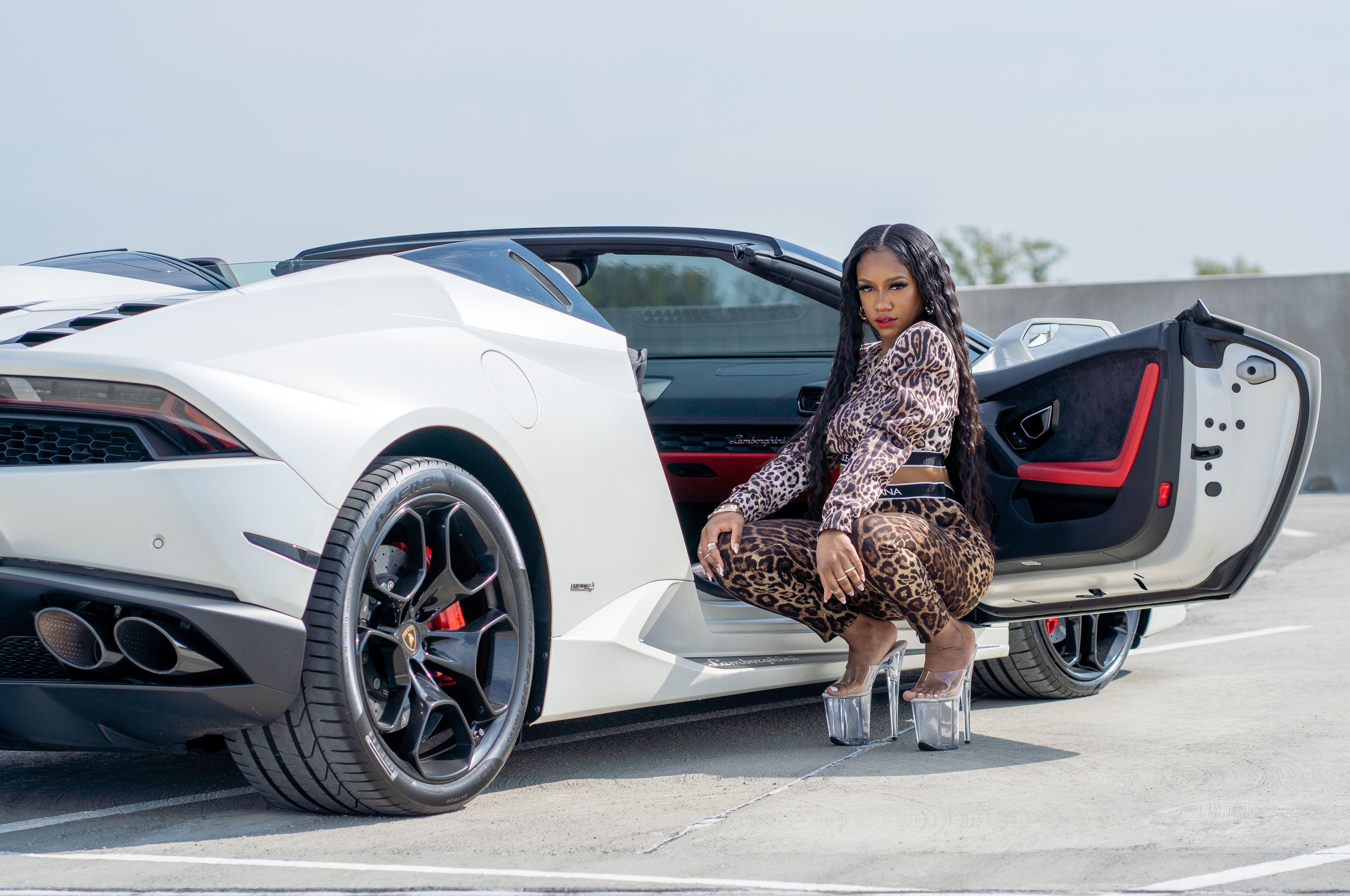 Fashionable woman in leopard print outfit by a white Lamborghini on a sunny day.