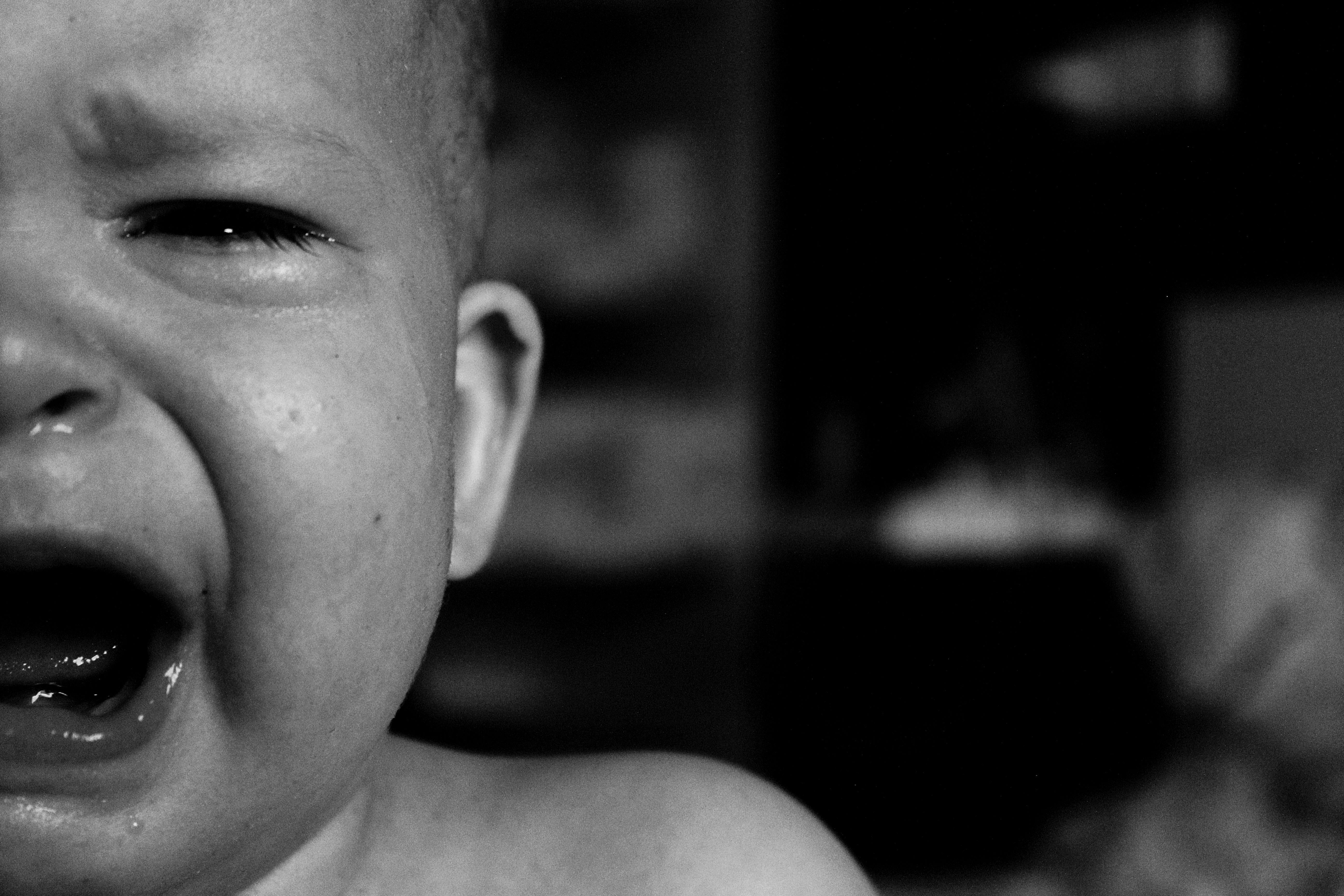 Emotional close-up of a crying baby's face captured in black and white with a blurred background.
