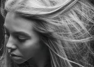 Black and white close-up portrait of a woman with wind-swept hair, capturing emotion and movement.