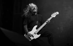 Dynamic black and white photo of an adult male musician with long hair playing a bass guitar passionately.