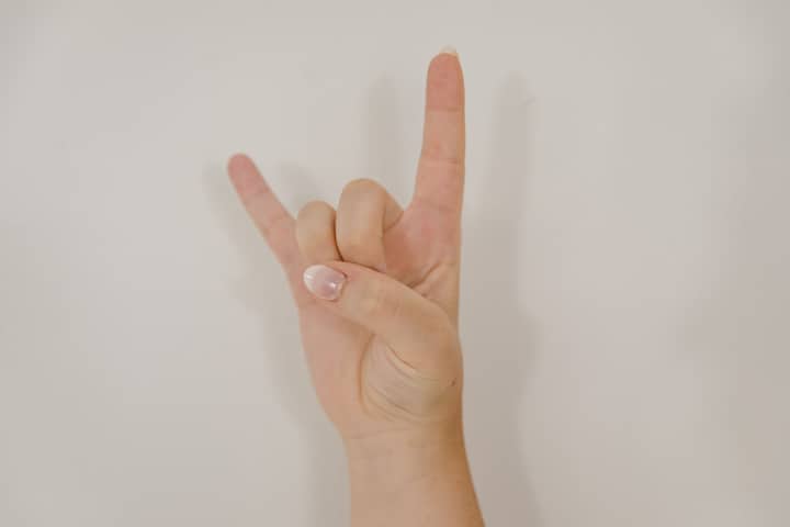 Close-up of hand making 'I Love You' gesture in American Sign Language against white background.