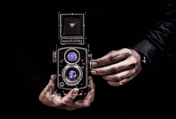 Close-up of hands holding a classic vintage Rolleicord camera against a dark background.