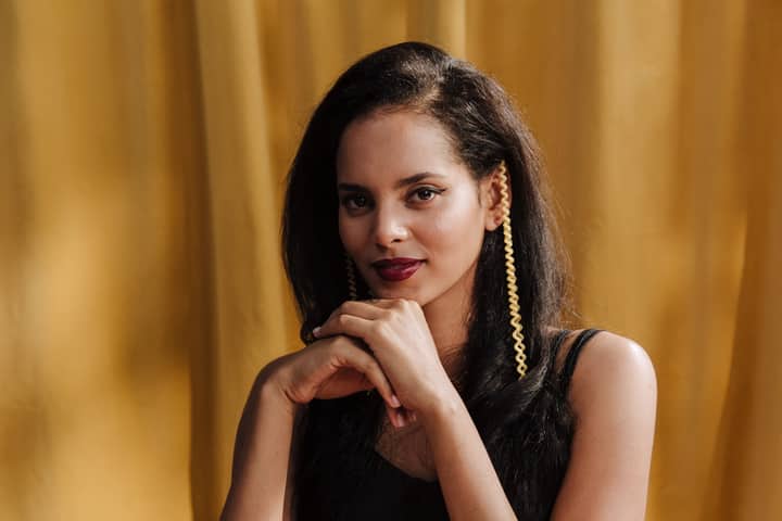 Portrait of a young woman with red lips and earrings in a yellow background studio setting.
