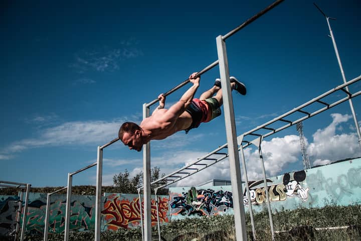An athletic man doing a flag pose on outdoor gym bars with a graffiti wall backdrop.