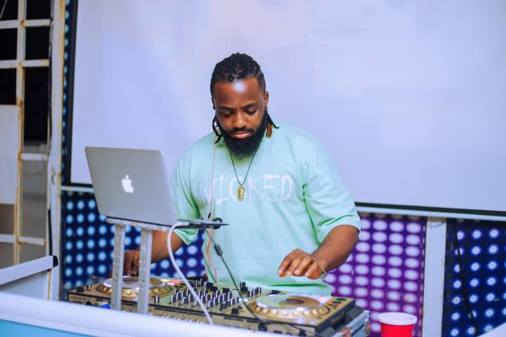 DJ performing with mixer and laptop at an indoor music event in Lagos, Nigeria.
