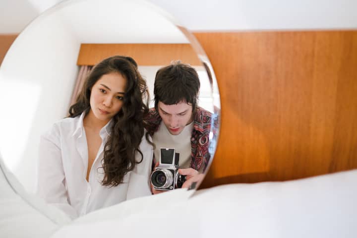 Intimate portrait of a couple using a vintage camera reflected in a mirror indoors.