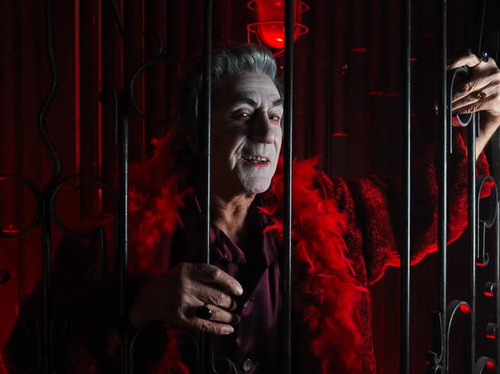 A spooky vampire in a red costume behind bars, perfect for Halloween and festive themes.