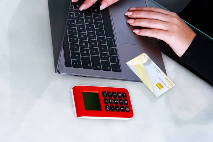 Hands using laptop with credit card and security device for online payment, emphasizing cybersecurity.