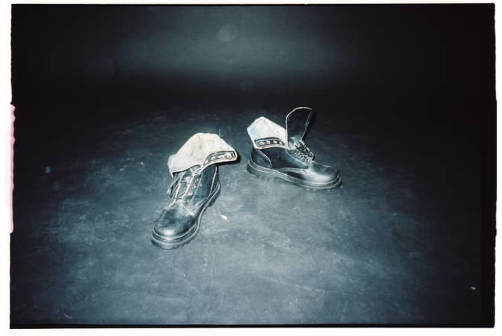 Close-up of black leather boots on a dusty floor under spotlight.
