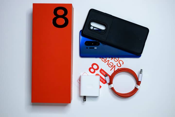 Flatlay of OnePlus 8 Pro with accessories on white background, showcasing packaging and contents.