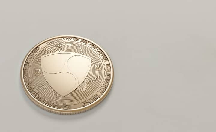 Close-up of a golden NEM cryptocurrency coin on a neutral background.