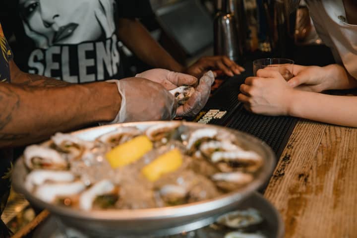 Close-up of fresh oysters being prepared at a bar counter with lemons on ice.