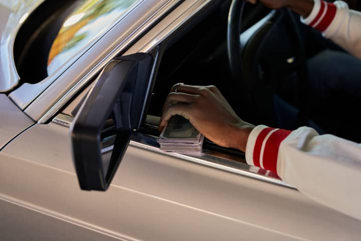 A close-up view of a hand holding cash through a car window, capturing a candid moment.