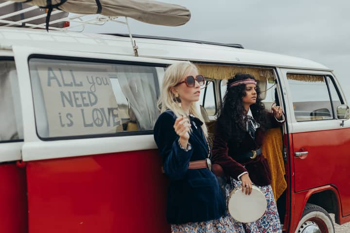 Two women in bohemian outfits by a vintage VW campervan on an adventurous road trip.