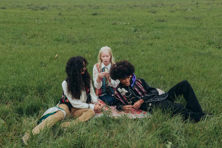 Three young adults enjoying a relaxing time on a picnic blanket in a grassy field, embracing nature and friendship.