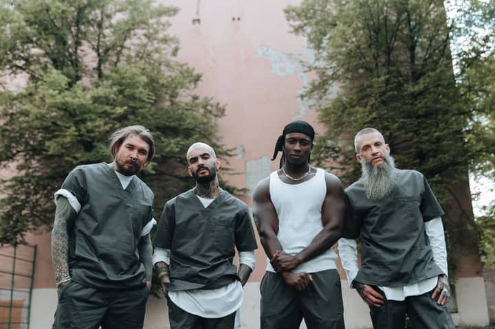 Four men in prison attire standing outdoors with a serious expression.