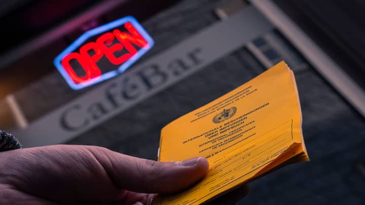Close-up of a hand holding a vaccination card in front of a cafe bar with an open sign.