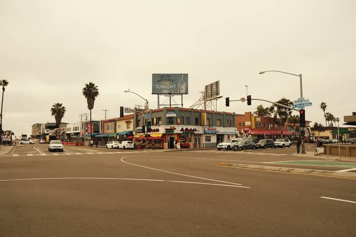 Vibrant city intersection featuring palm trees, shops, and cars under an overcast sky.