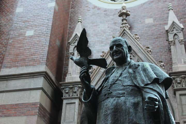 Bronze statue of Pope John XXIII with a dove, against a historic brick wall in İstanbul, Turkey.