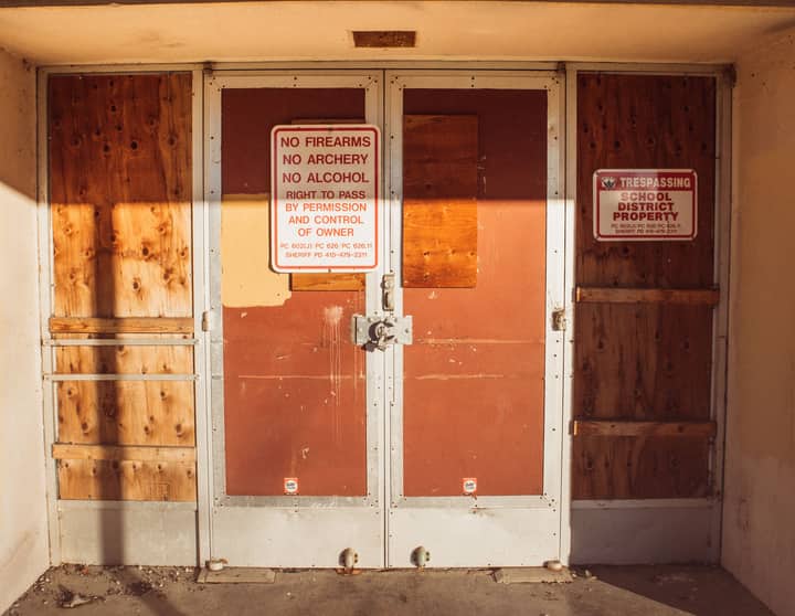 A locked and boarded school entrance with no trespassing signs emphasizing safety rules.