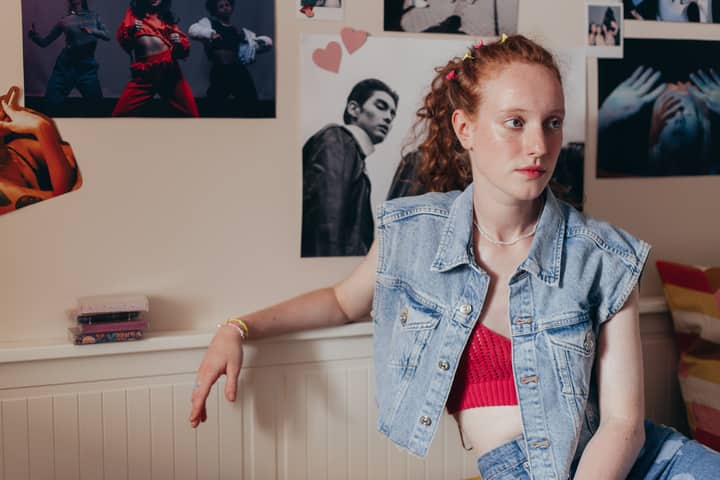 Teenage girl in a denim vest relaxing in a stylishly decorated room with artistic posters.