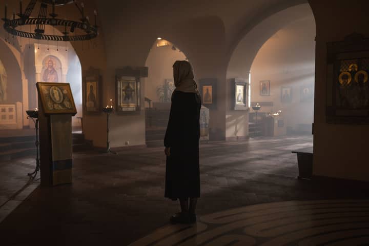 A contemplative scene inside a church with a woman standing among religious icons.