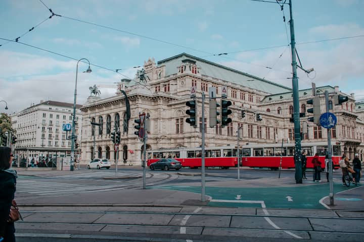 Elegant Vienna State Opera with red tram passing by, capturing the essence of Vienna's historic charm and modern city life.