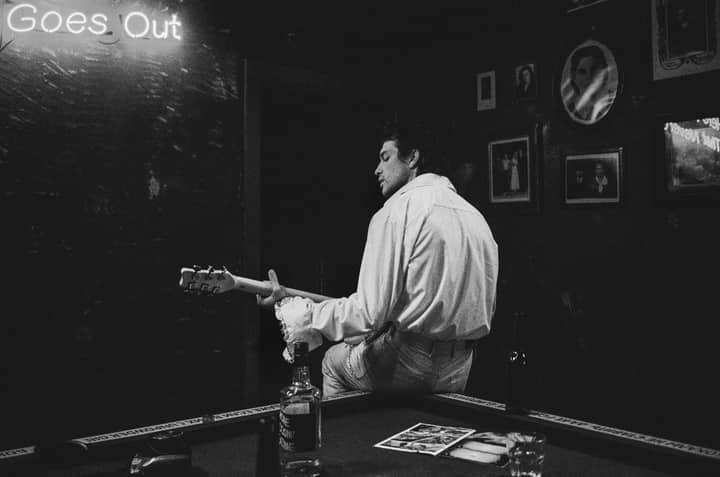 A musician at a bar playing guitar with a moody atmosphere in black and white.