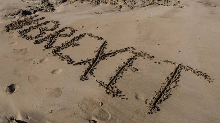 'Brexit' inscribed on sandy beach with footprints around it.