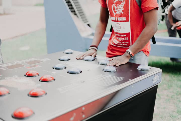 Group of young adults enjoying outdoor arcade buttons game in a park setting.