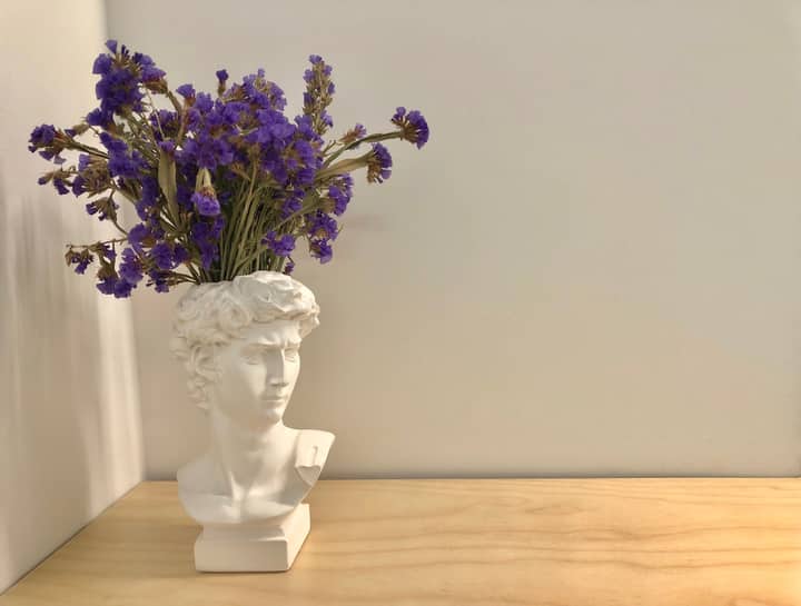 A decorative bust vase with purple flowers on a wooden table, minimalist design.