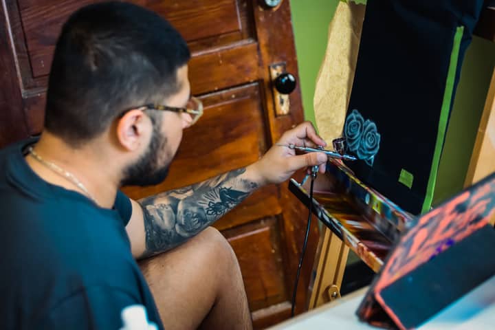 A tattoo artist skillfully uses an airbrush to create intricate rose artwork indoors.