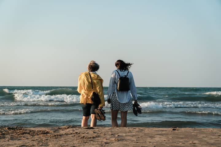 A mother and daughter walk on the sandy seashore at sunset, enjoying the ocean waves.