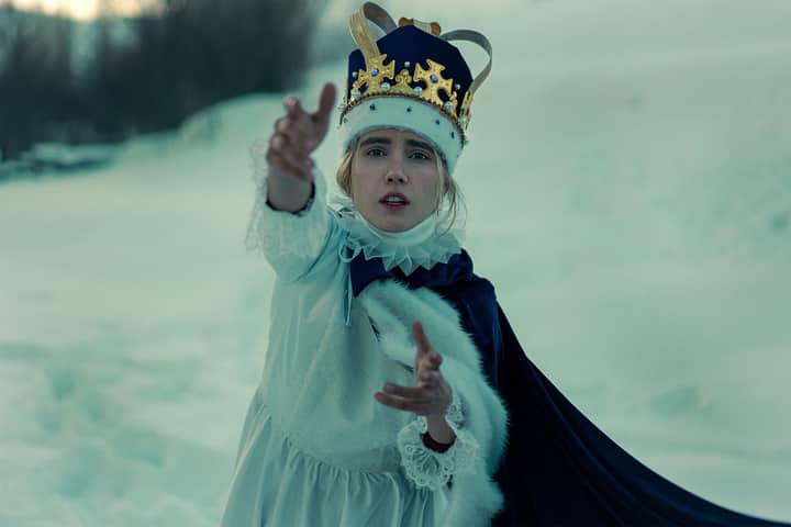 A woman dressed in a royal costume with a crown, standing in a snowy winter landscape, exuding elegance and mystery.