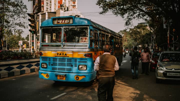 A blue bus in an urban environment with pedestrians and traffic on a city street.