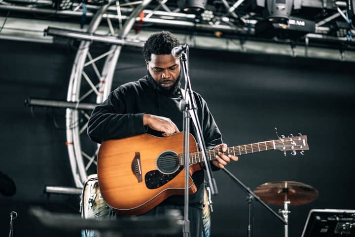 A male musician tuning his guitar on stage before a live performance.