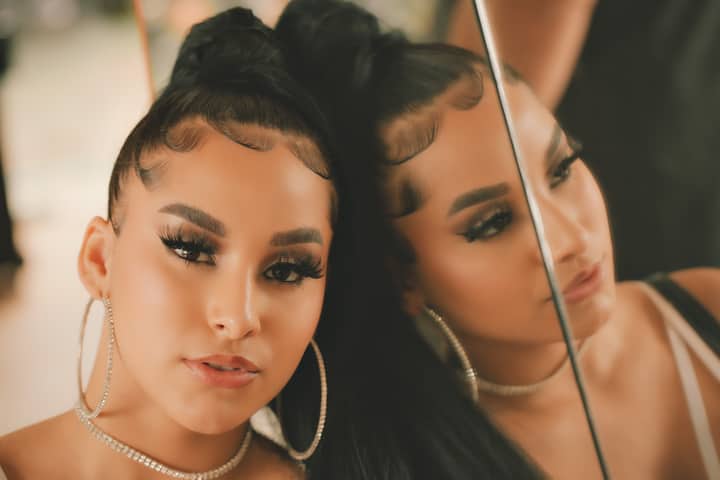 Close-up portrait of a woman with hoop earrings and makeup, reflected in a mirror.