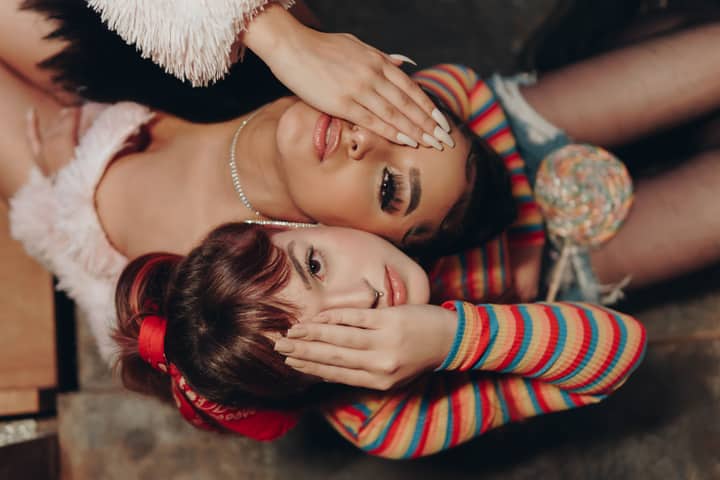 Two fashionable women lying down with playful poses, expressing youthful vibes and modern style indoors.