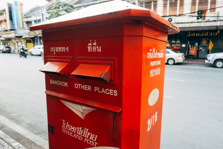 Vibrant red postal box in Bangkok, Thailand, with street in background.