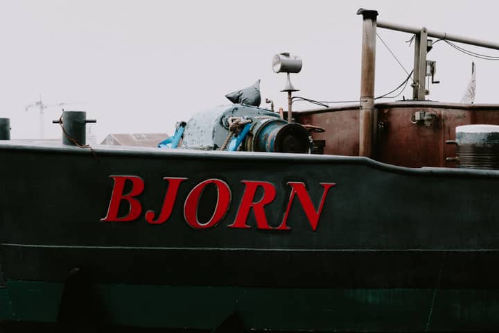 Close-up of a rustic boat with 'BJORN' text, conveying an industrial vibe against a cloudy backdrop.
