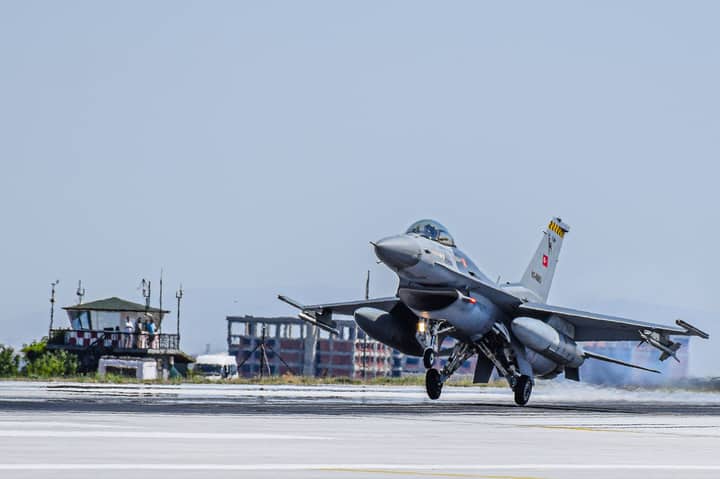 A military fighter jet taking off from an airport runway under a clear blue sky.