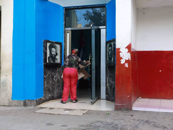 A person carrying cardboard boxes enters a blue and red building with portraits on the walls.