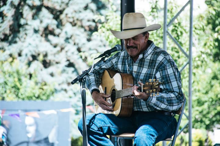 Cowboy musician performing on stage with guitar outdoors. Captured during daytime.